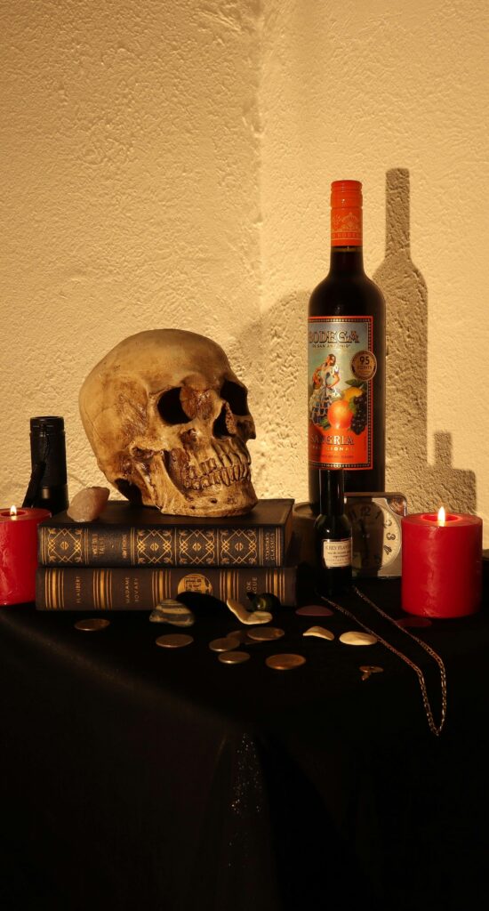A dark and moody still life featuring a skull, candles, books, and a wine bottle, evoking a mysterious atmosphere.